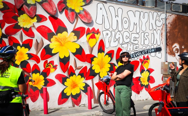 Electro-bici riders stop in front of a mural in Pacoima