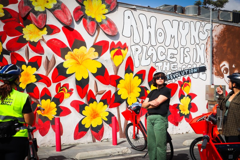 Electro-bici riders stop in front of a mural in Pacoima